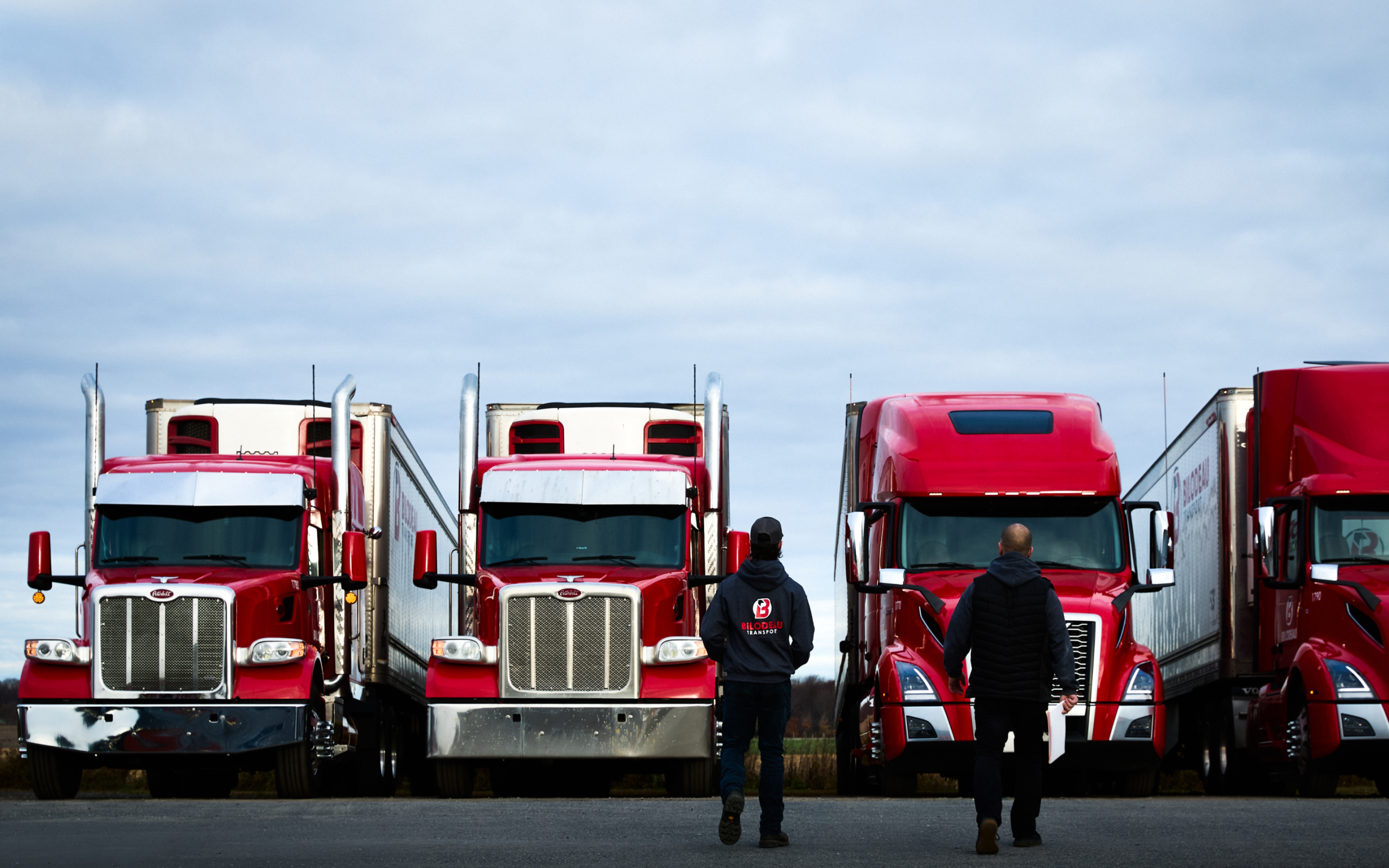 2 hommes se tenant devant 4 camions aux couleurs de Bilodeau Transport